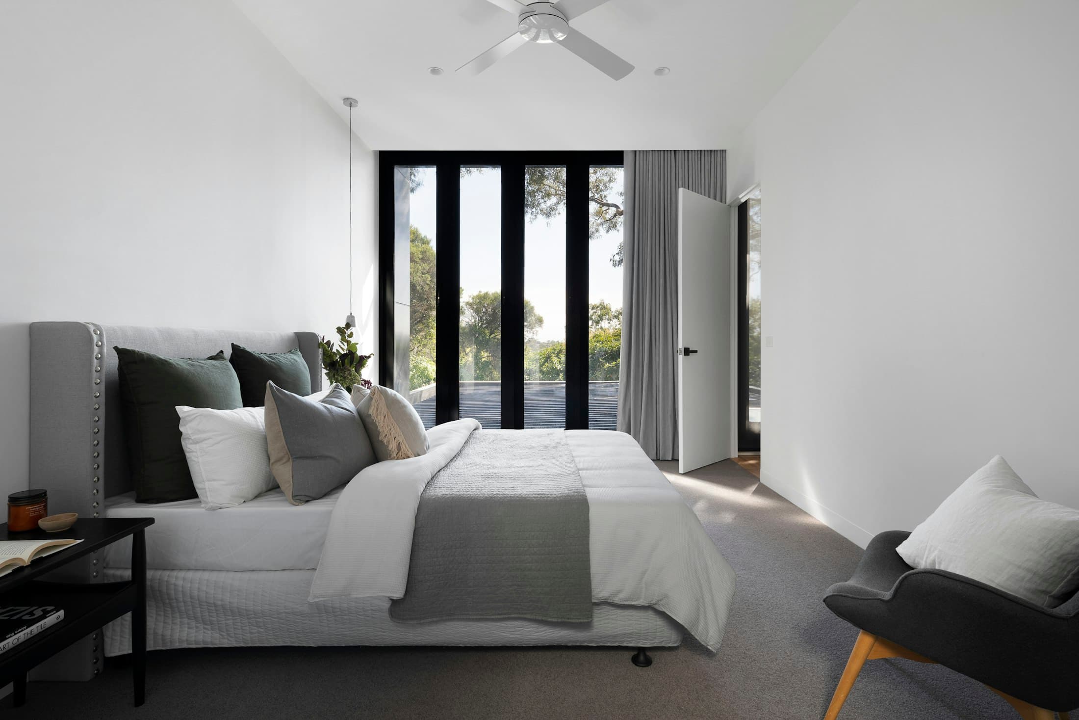 A bedroom on the hillside wing. Black steel-framed glazing opens the room to a private patch of garden.